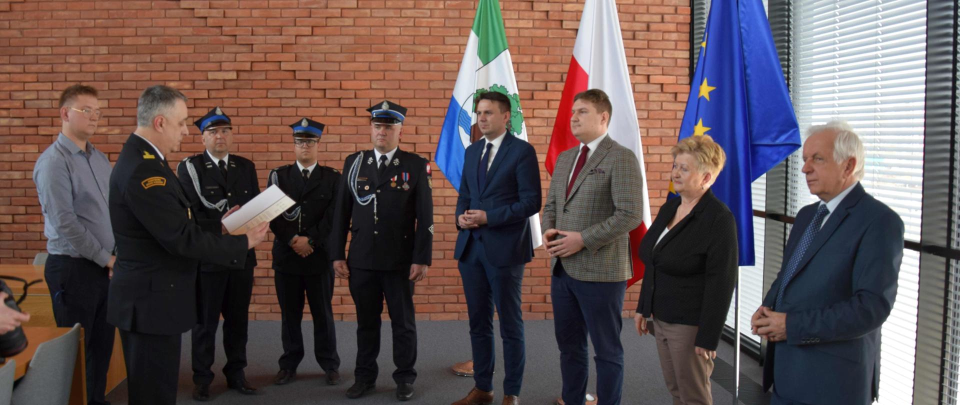 Komendant Powiatowy PSP odczytuje treść promesy. W tle przedstawiciele OSP Słomczyn, władz samorządowych i rządowych. 