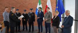 Komendant Powiatowy PSP odczytuje treść promesy. W tle przedstawiciele OSP Słomczyn, władz samorządowych i rządowych. 