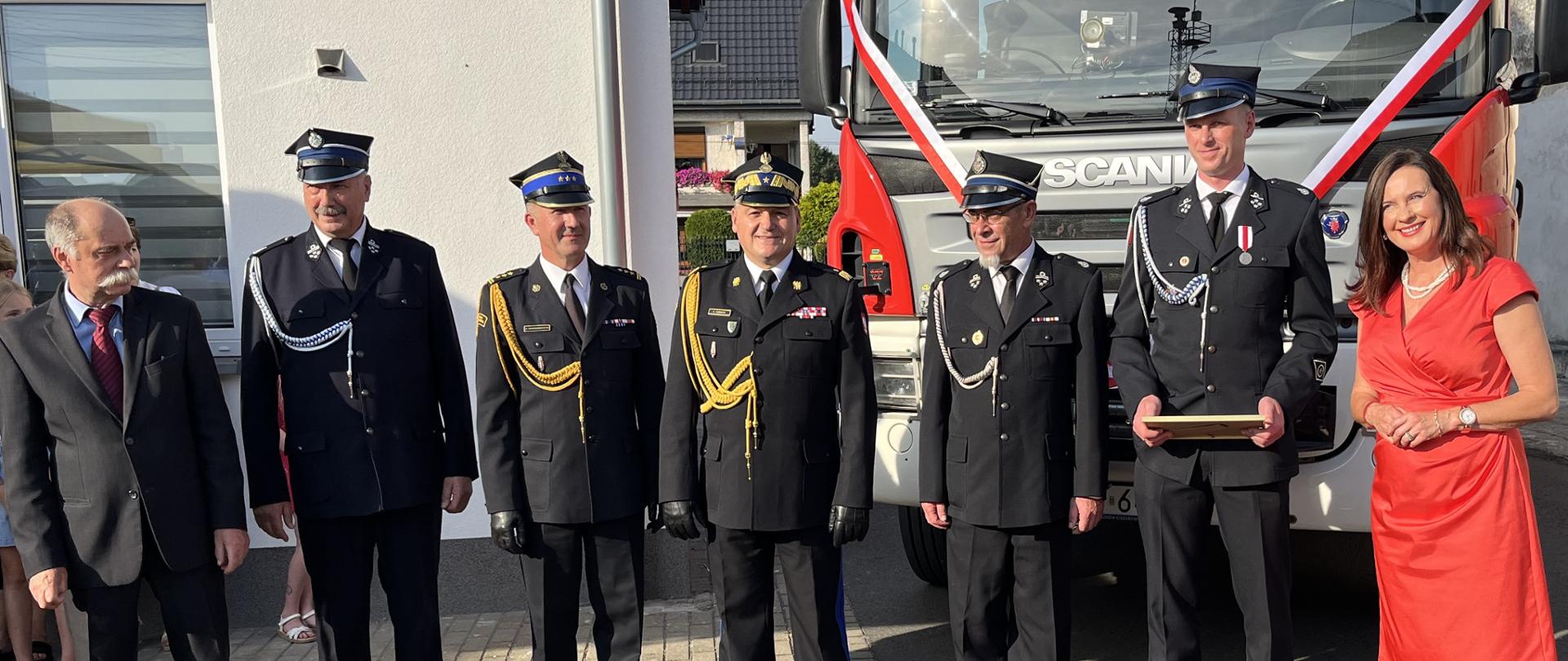 Wspólne zdjęcie przedstawicieli OSP Dębska Kuźnia oraz zaproszonych gości na tle przekazywanego samochodu pożarniczego.