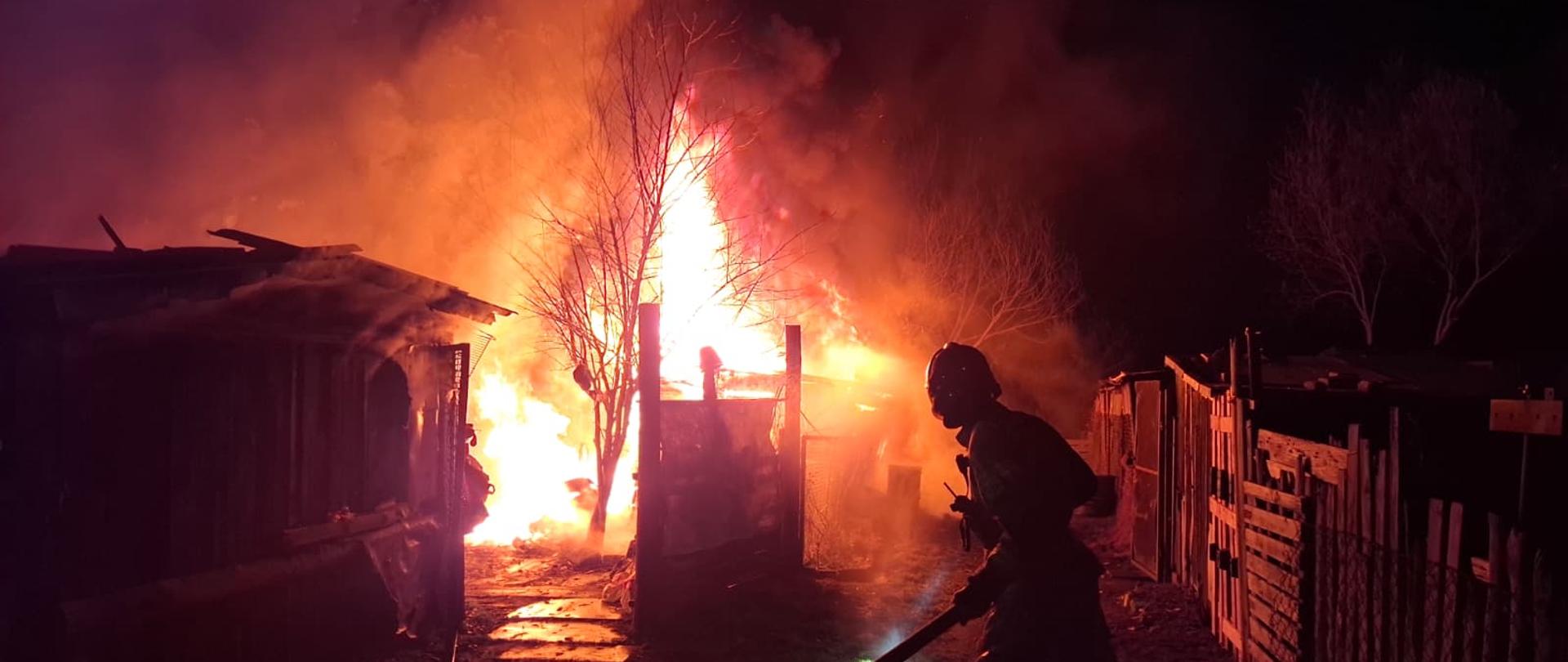 Na zdjęciu widać strażaka podczas działań i w tle pożar 