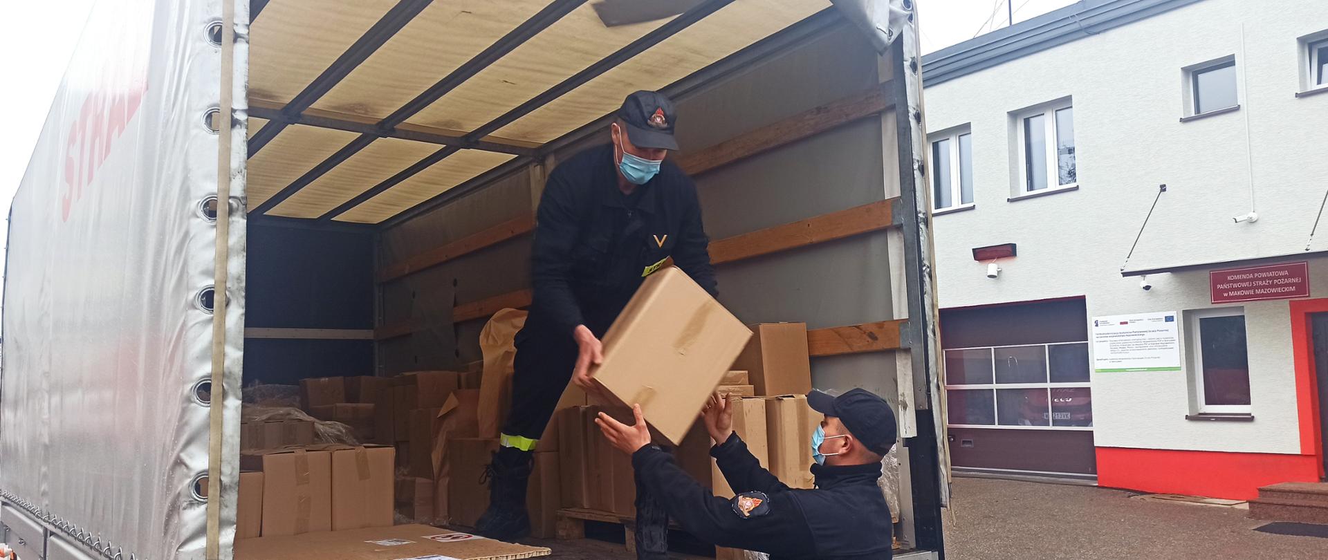 Dystrybucja ulotek. Dwóch strażaków wypakowujących kartonowe pudła z samochodu ciężarowego.