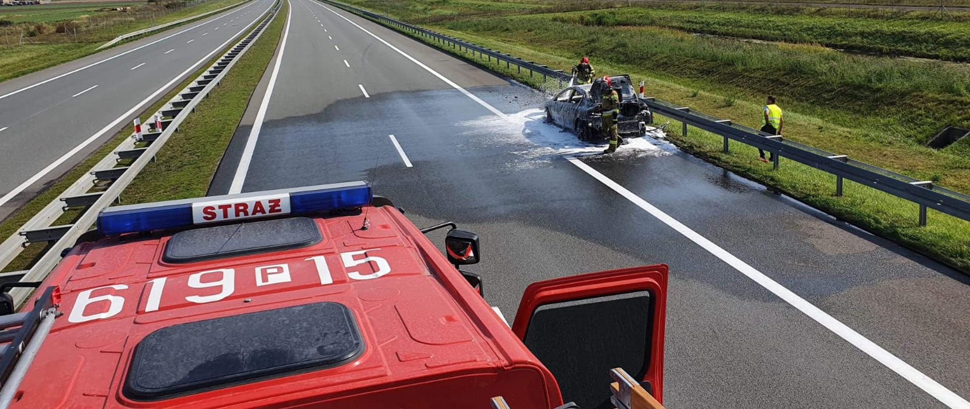 Strażacy przy użyciu piany gaśniczej gaśniczej gaszą samochód stojący na jezdni