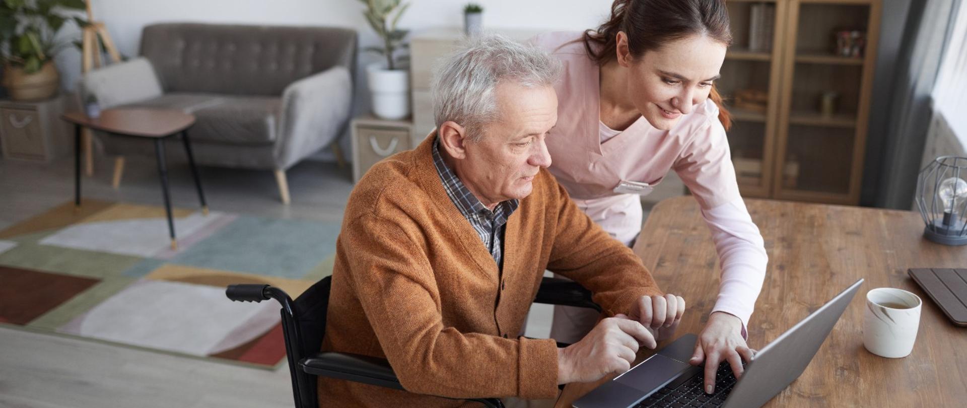 dwie osoby przed laptopem, mężczyzna siedzi na wózku inwalidzkim