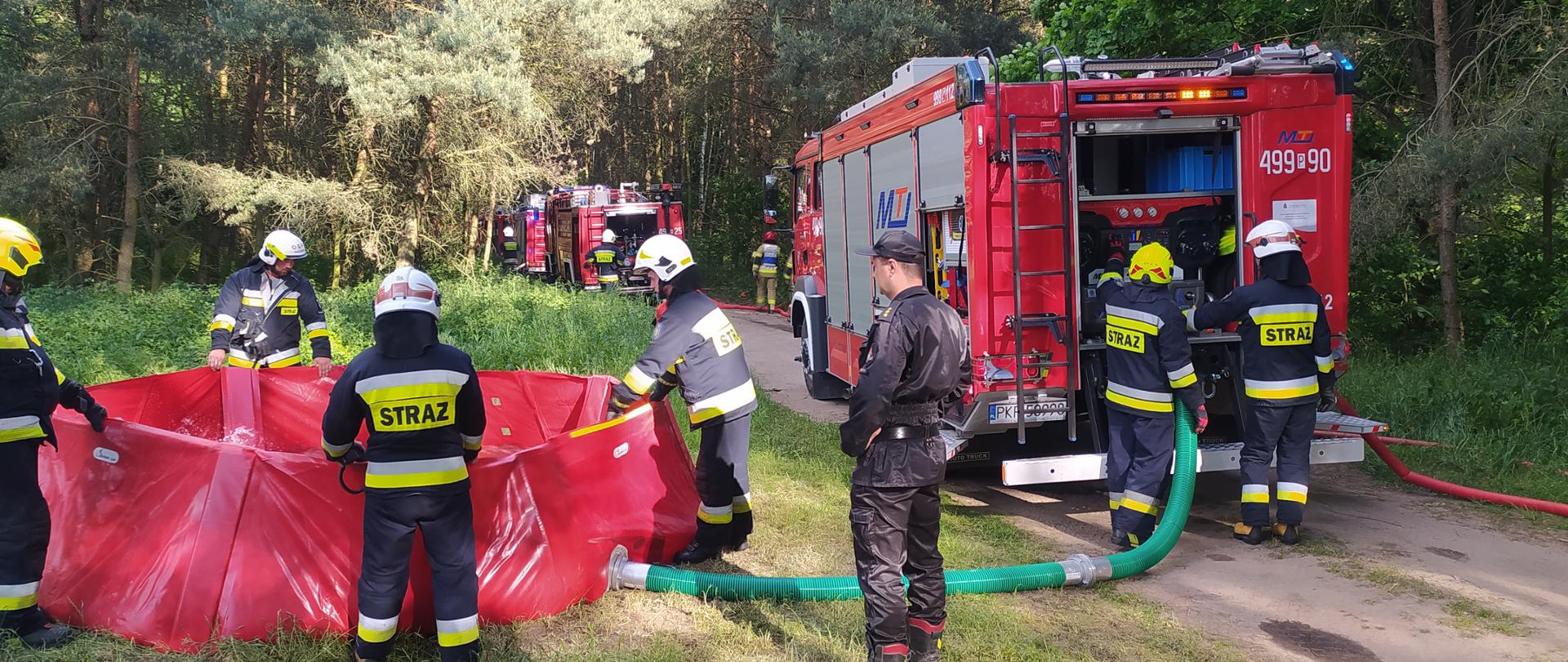 Strażacy sprawiają zbiornik stanowiący bufor wody do zasilania wozów bojowych. każdy strażak trzyma krawędź zbiornika do momentu napełnienia go wodą. Całość ocenia obserwator z ramienia Komendy Powiatowej.