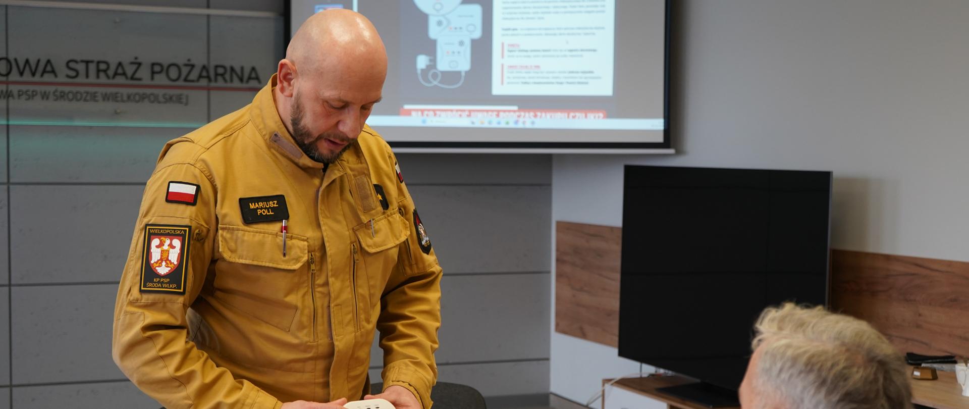 Zastępca Dowódcy JRG prezentuje działanie czujki czadu i omawia zasady bezpieczeństwa w domu związane z okresem grzewczym i występowaniem czadu i dymu.