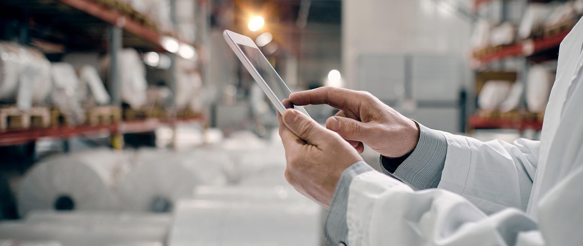 Tablet trzymany w obu dłoniach przez człowieka.