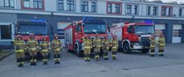 Minuta ciszy dla poległych strażaków z Ukrainy - zdjęcie przedstawia strażaków oddających hołd poległym strażakom w tle samochody pożarnicze oraz budynek Komendy