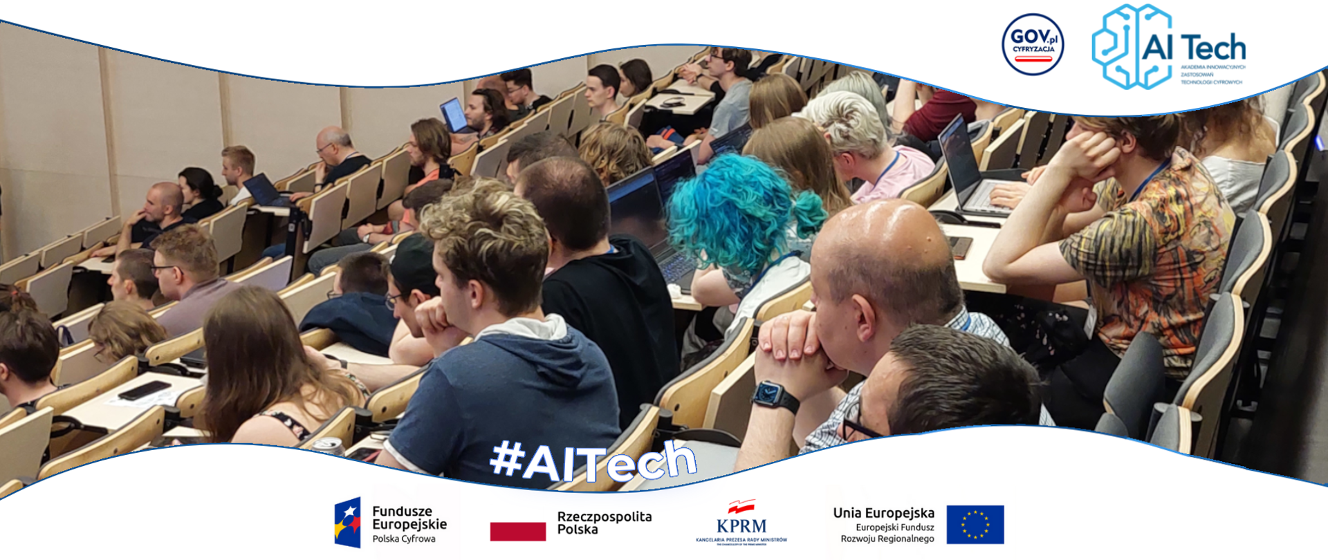 Studentki i studenci podczas wykładu. Logotypy projektowe znak FE, barwy RP, znak KPRM, znak UE.