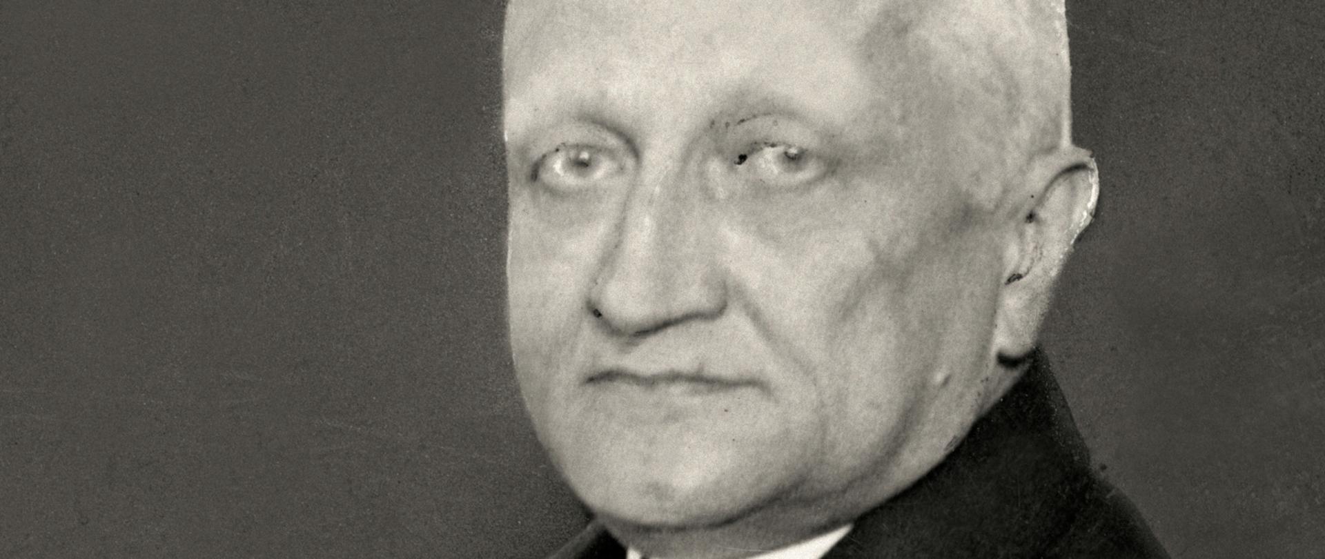 Konstanty Skirmunt - czarno-biały portret mężczyzny, siwe włosy, jasne oczy, ciemna marynarka, jasny krawat, biała koszula - półprofil.