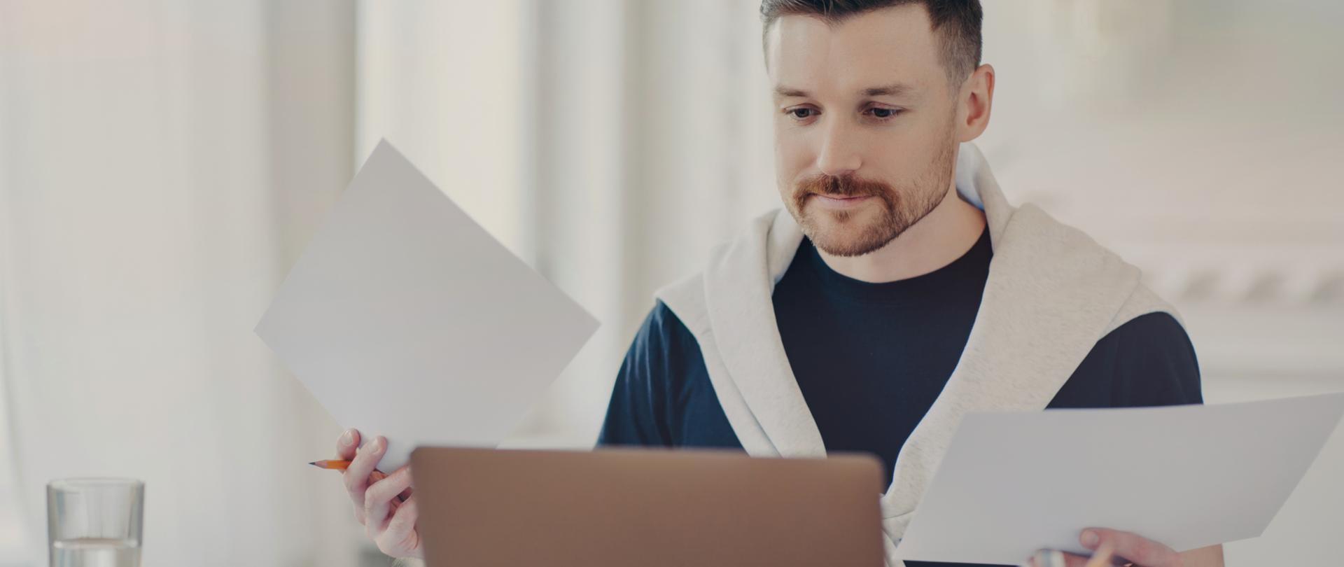 Busy freelancer in casual wear analyzes project results, works remotely from home office, multitasking with computer and paperwork. Embracing freelance and business concepts.