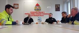 Na zdjęciu widać 7 osób siedzących przy stole na sali konferencyjnej w Komendzie Miejskiej PSP w Świnoujściu. Od lewej pracownik Gaz-System, Komendant Miejski PSP, Zastępca Komendanta Miejskiego PSP, Dowódca JRG 2, pracownik Gaz-System. W tle ściana, od lewej strony godło RP, logo PSP wraz z napisem pod logiem KOMENDA MIEJSKA PSP w Świnoujściu, Toporek strażacki z grawertonem.