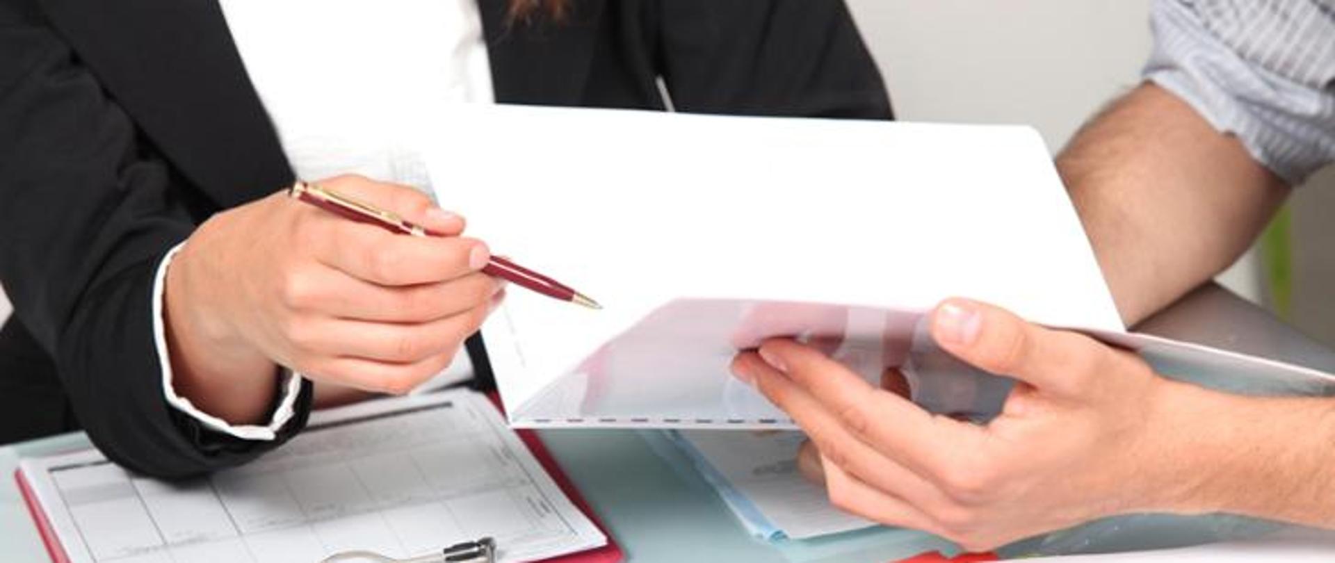 Dwie osoby trzymające w rękach dokumenty i długopis.