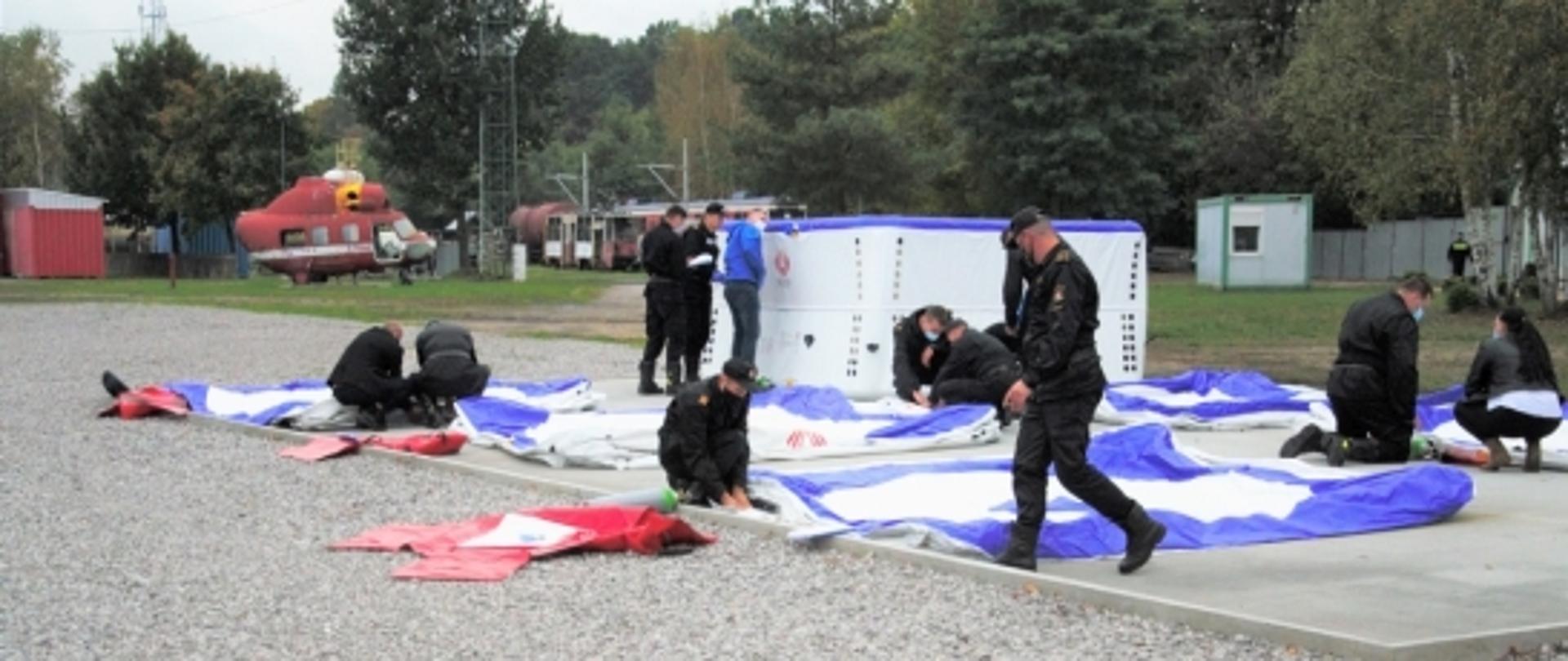 Strażacy dokonujący przeglądu nowych skokochronów rozłożonych na ziemi.