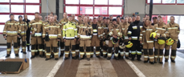 Na zdjęciu znajdują się strażacy w nomexach ustawieni do zdjęcia w garażu