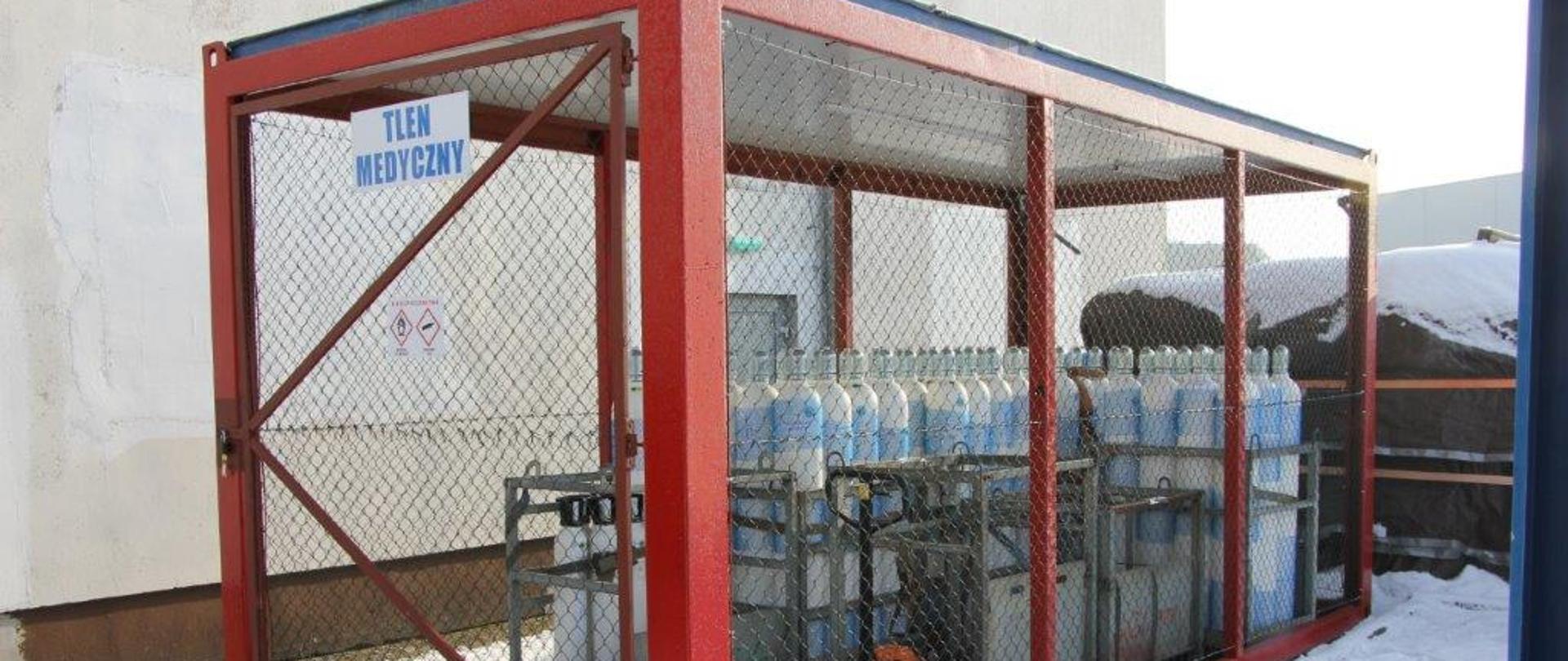 za zamkniętym ogrodzeniem z siatki widoczne butle z tlenem