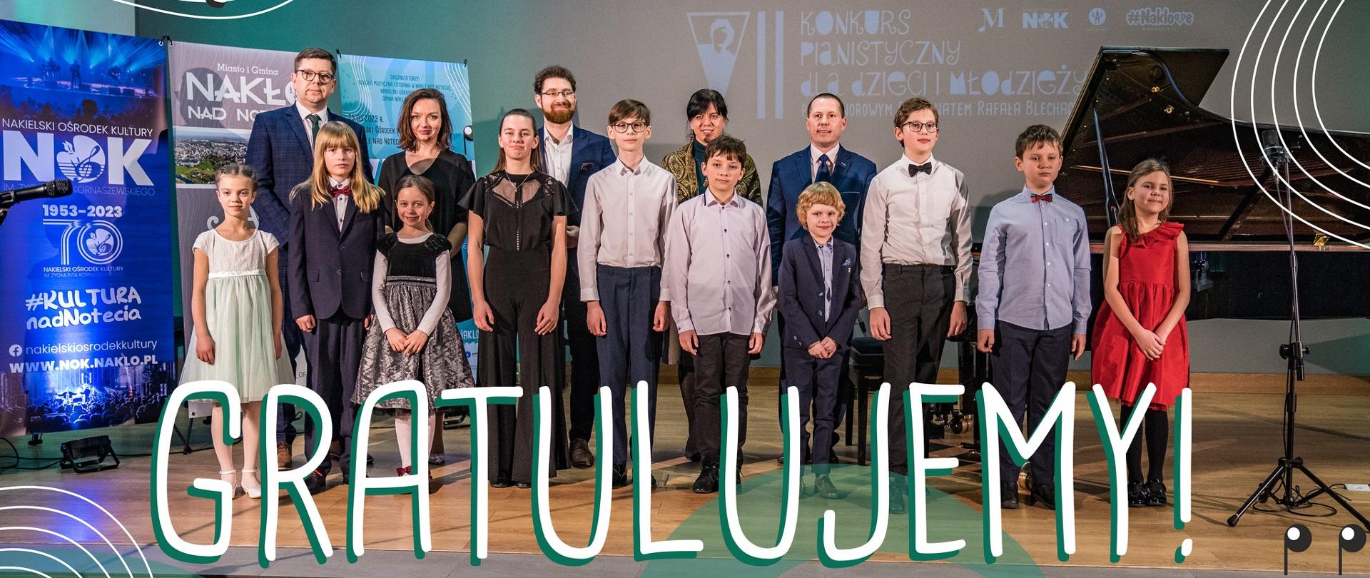 Na scenie wszyscy laureaci, jury oraz organizatorzy VII Konkursu Pianistycznego dla dzieci i młodzieży pod honorowym patronatem Rafała Blechacza. Po lewej stronie bannery reklamowe, po prawej stronie czarny, koncertowy fortepian. W tle na ścianie napis: "koncert finałowy VII Konkursu Pianistycznego dla dzieci i młodzieży pod honorowym patronatem Rafała Blechacza. Po lewej stronie na pierwszym planie duży napis: "dziękujemy", u dołu "gratulujemy". Na samym dole grafika banneru reklamowego VII Konkursu Pianistycznego dla dzieci i młodzieży pod honorowym patronatem Rafała Blechacza z napisem w środku "do zobaczenia"