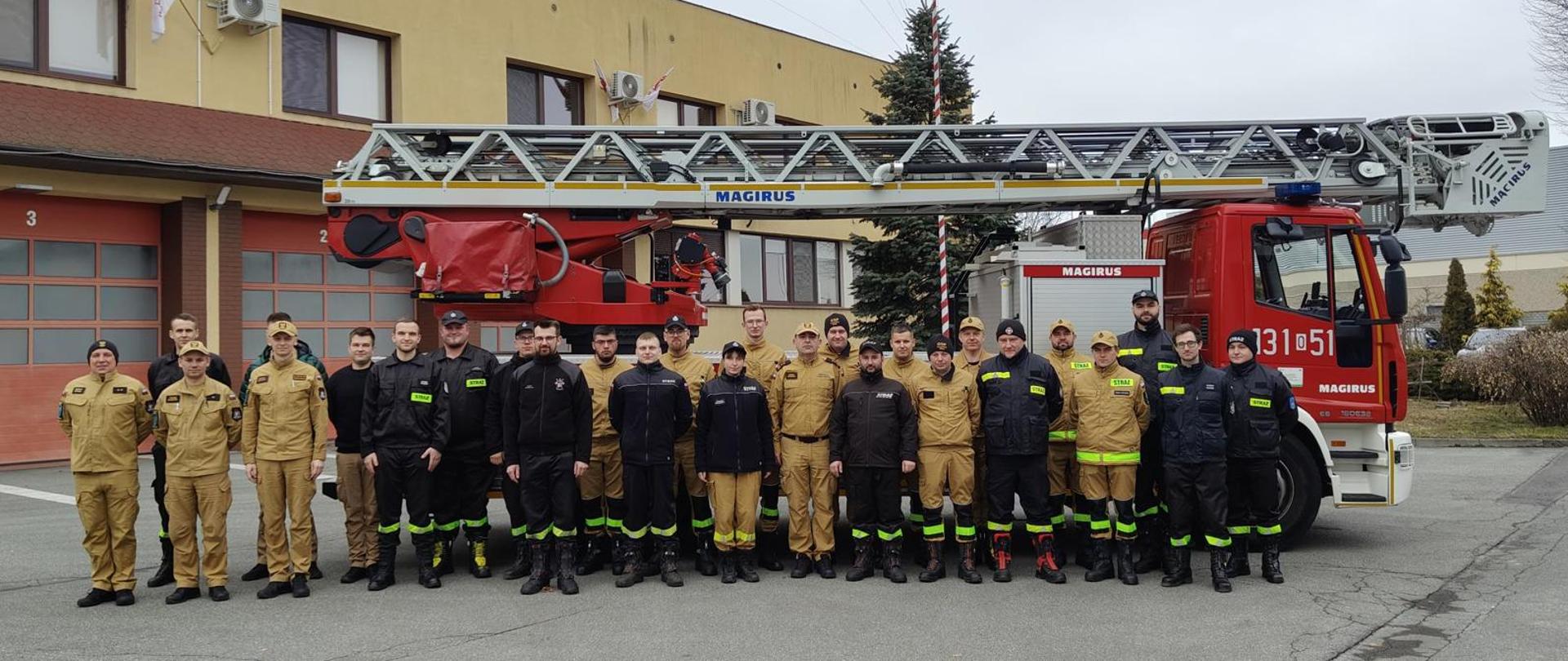 W dniach od 21.02.2025 r. do 02.03.2025 r. odbyło się szkolenie ,,Kierującego Działaniem Ratowniczym dla strażaka ratownika Ochotniczych Straży Pożarnych" realizowane przez KW PSP w Opolu na bazie KP PSP w Kluczborku zorganizowane dla druhów z powiatu kluczborskiego. Słuchacze zgłębili wiedzę dotyczącą funkcjonowania KSRG, praw i obowiązków KDR-a, kierowania działaniem ratowniczym, a także zasad łączności.
Do egzaminu przystąpiło 23 druhów. Wszystkie osoby zaliczyły egzamin pozytywnie.
Kursanci w ubraniu koszarowym a strażacy PSP w ubraniu służbowym stoją do wspólnego grupowego zdjęcia na tle drabiny mechanicznej i siedziby Komendy Powiatowej PSP w Kluczborku.