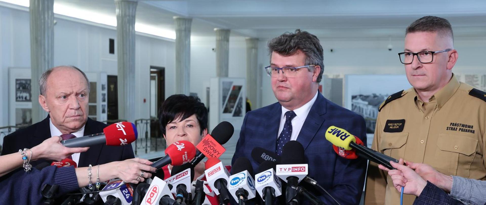 Zdjęcie przedstawia wiceministra Macieja Wąsika podczas konferencji prasowej w sejmie, po jego lewej stronie stoi zastępca Komendanta Głównego nadbrygadier Krzysztof Hejduk w nowym wzorze umundurowania służbowego strażaków PSP. 