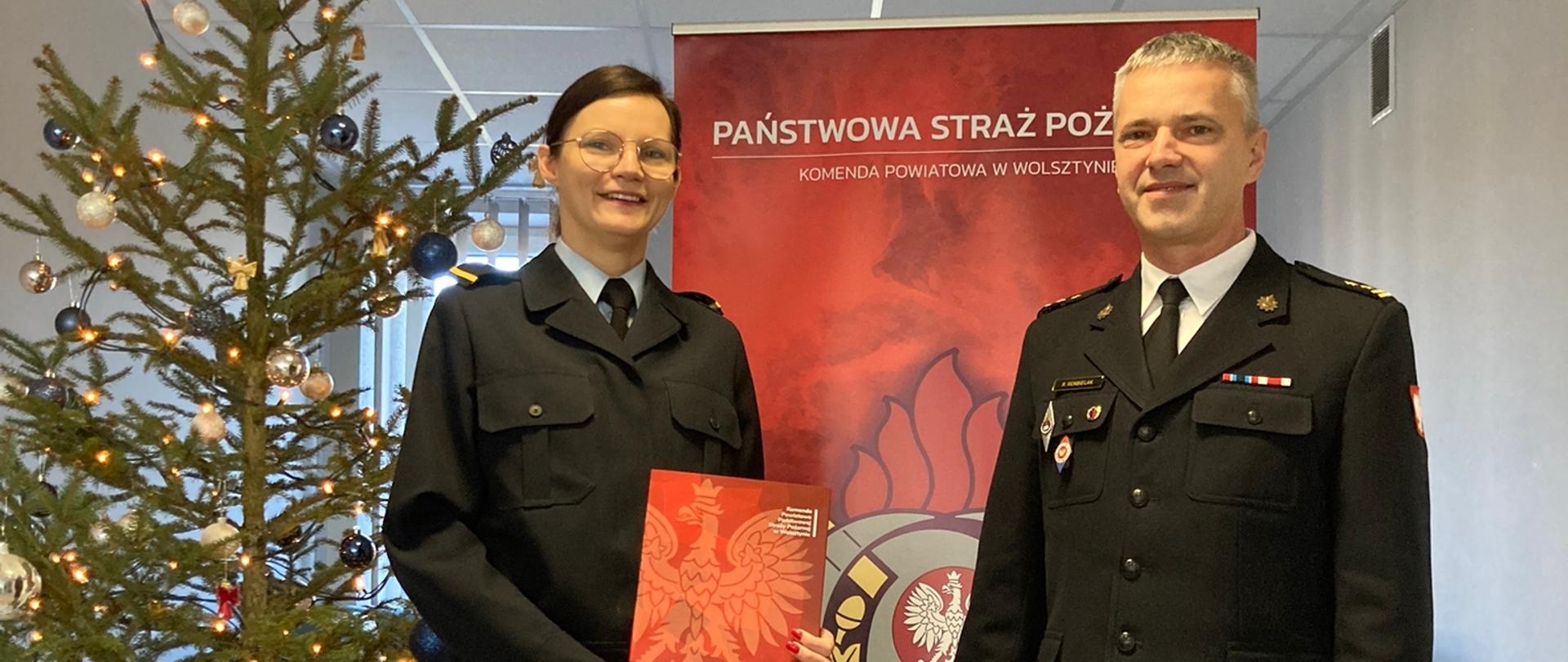 Funkcjonariusz odbiera z rąk Komendanta decyzję o mianowaniu do służby stałej. W tle baner PSP oraz świąteczna choinka.