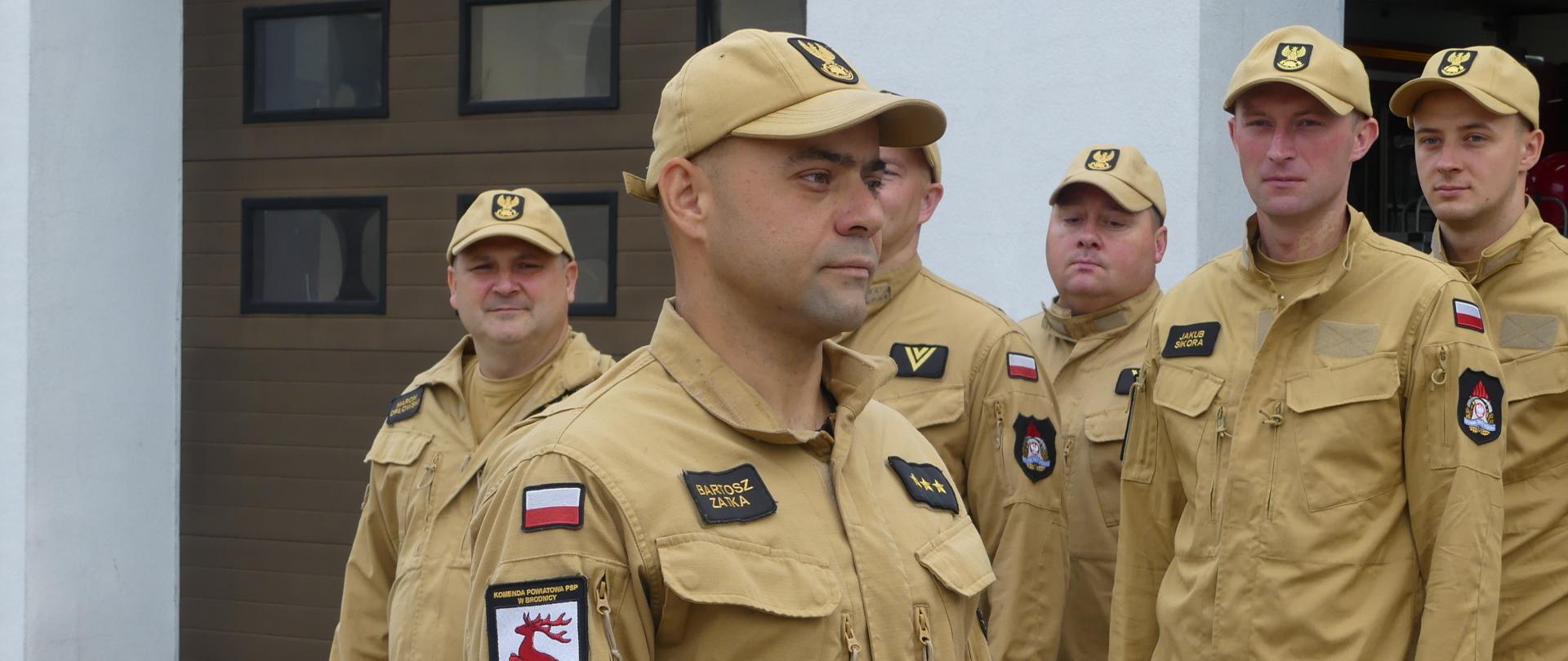 Zdjęcie przedstawia mianowanego na stanowisko dowódcy zmiany aspiranta sztabowego Bartosza Zatkę. Mianowany ubrany w umundurowanie służbowe koloru miodowego. Za nim w dwuszeregu stoją inni funkcjonariusze Komendy Powiatowej.