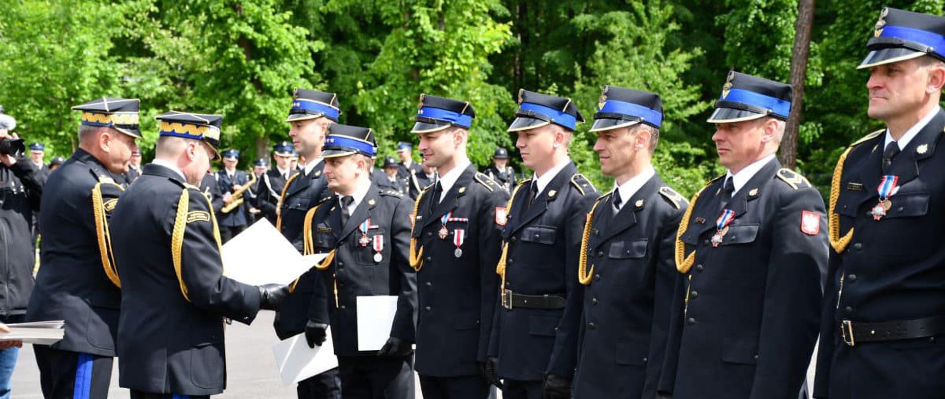 Zastępca KG PSP wręcza teczki z aktami nadania stopnia strażakom ustawionym w szeregu