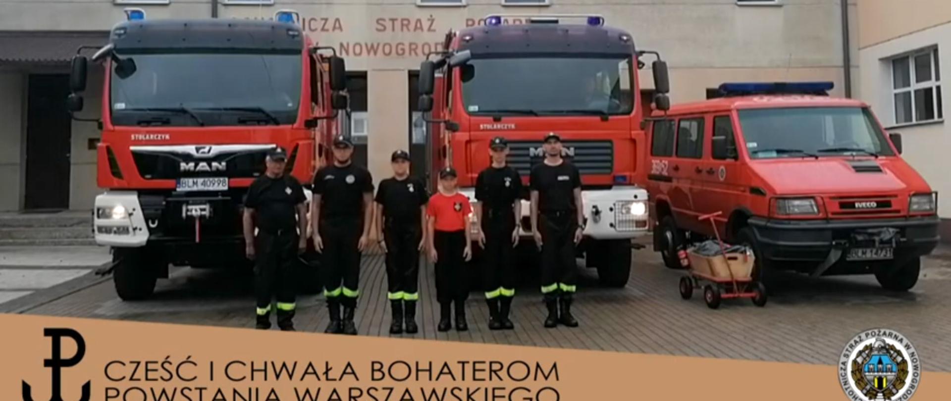 Strażacy w ubraniach koszarowych stoją przy trzech samochodach pożarniczych na terenie swojej jednostki OSP. Na zdjęciu widać również dwóch chłopców z "osiedlowej straży pożarnej" nie dawno założonej w Nowogrodzie.