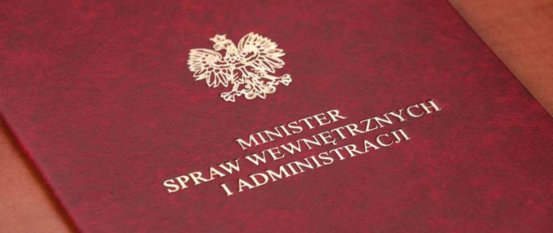 Zdjęcie przedstawia teczkę w kolorze czerwonym z godłem Polski i napisem: Minister Spraw Wewnętrznych i Administracji