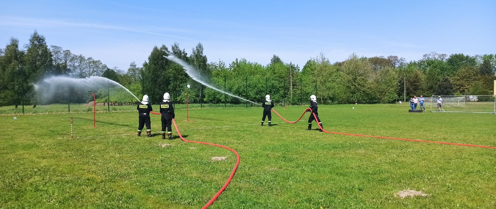 Po dwóch strażaków ochotników stoi na końcu linii gaśniczej, przodownik trzyma prądownicę, którą celuje w tarczę, do momentu, aż strumień wody przechyli tarczę. Natomiast pomocnik przodownika, stoi za nim z trzyma odcinek z wodą. Druhowie ubrani są w stroje koszarowe oraz mają białe hemy na głowie.
