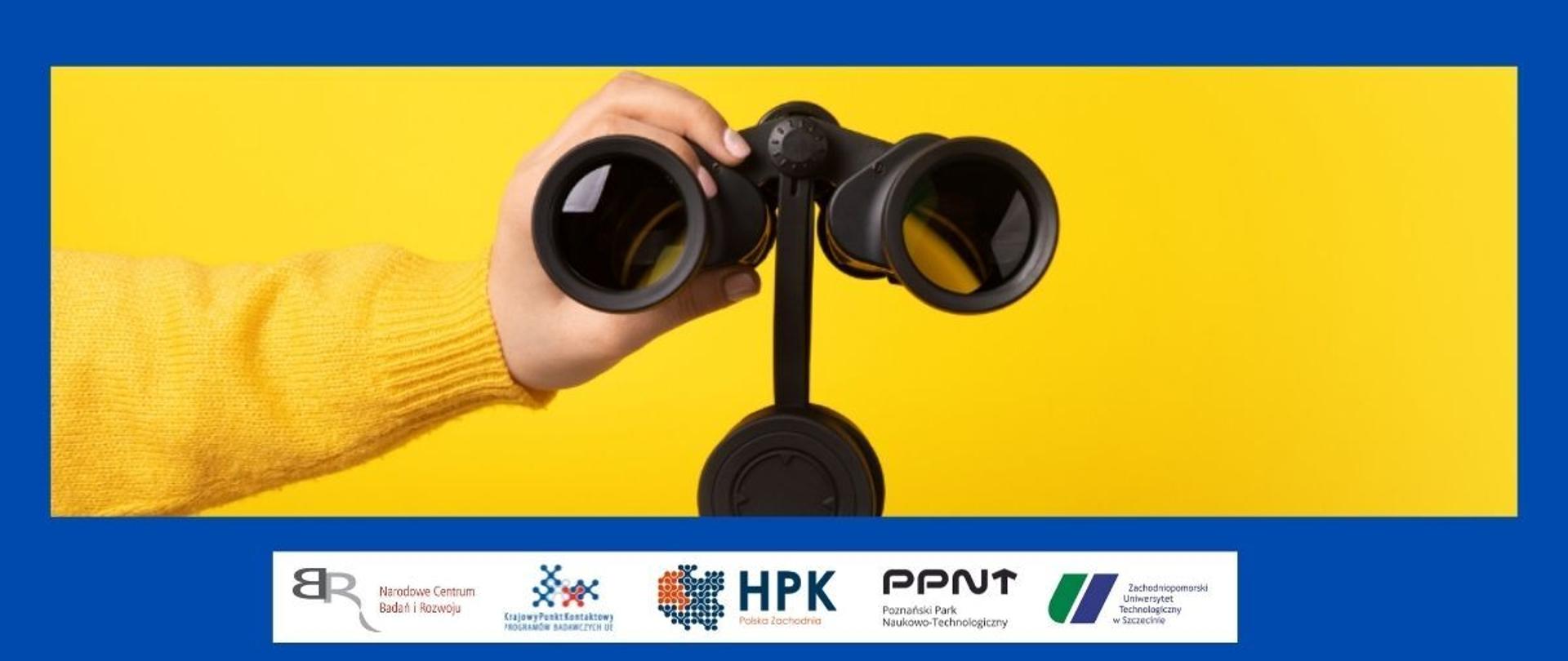 Ręka trzymająca lornetkę
na dole pasek logotypów