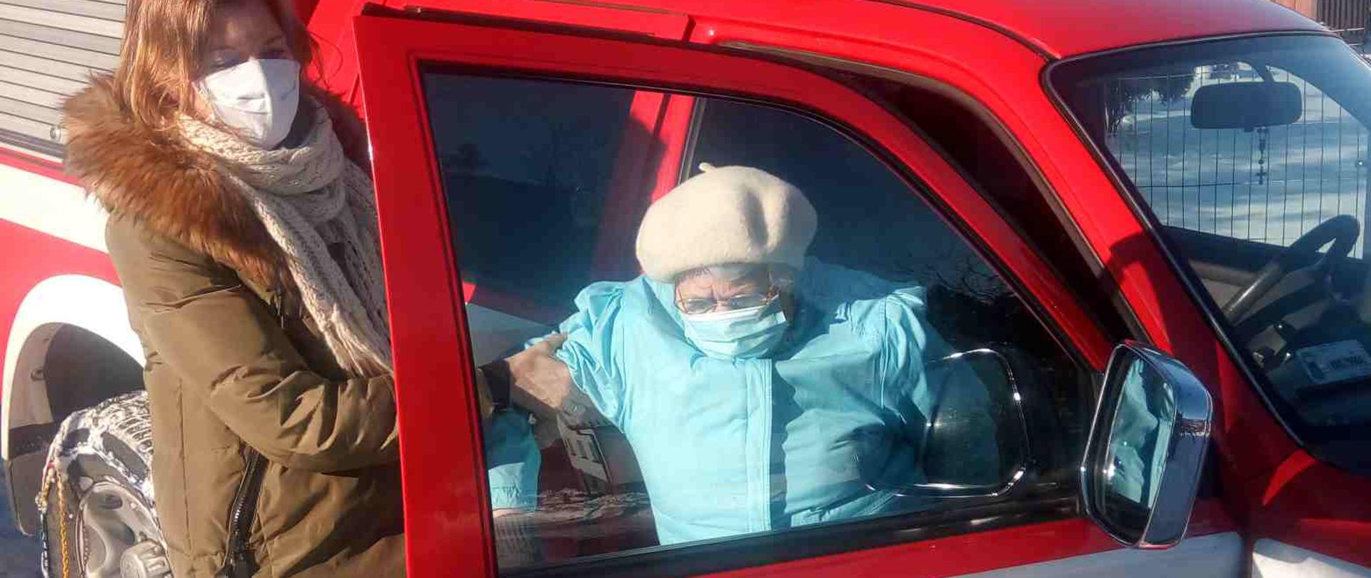 Osoba udająca się na szczepienie wysiada z samochodu pożarniczego. Druga osoba pomaga jej w wysidaniu