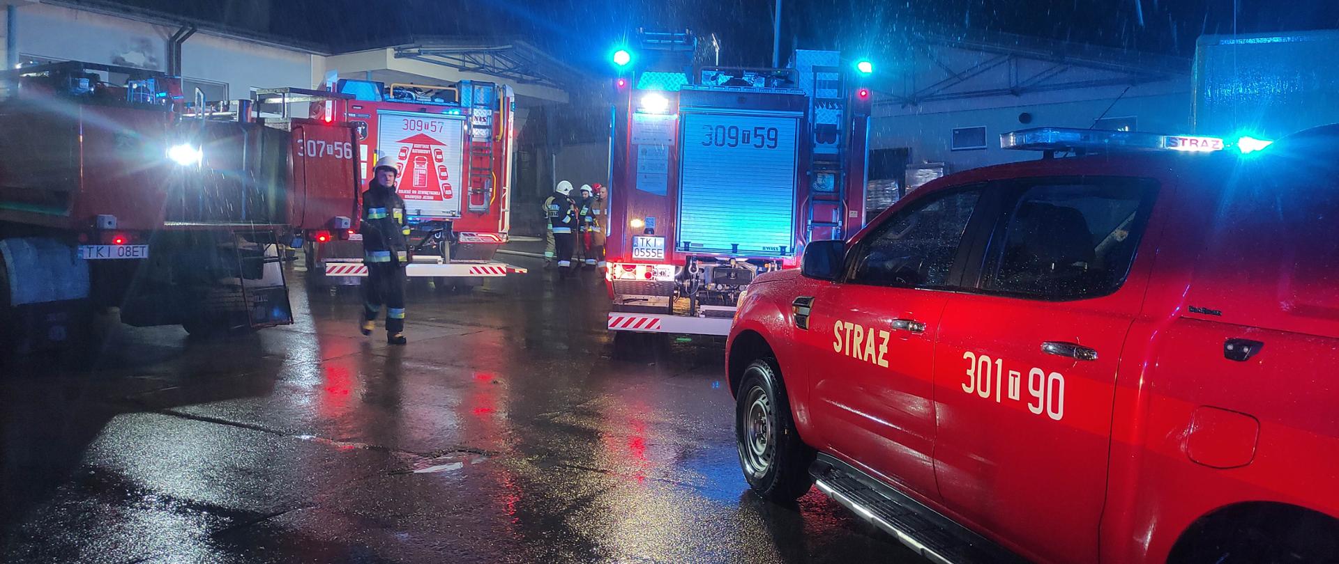 Zdjęcie przedstawia plac wewnętrzny piekarni na którym stoją cztery samochody pożarnicze oraz strażacy.