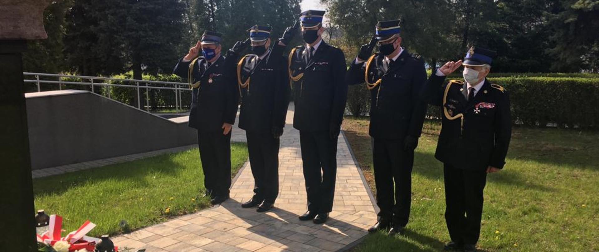 Zdjęcie przedstawia funkcjonariuszy w mundurach galowych podczas oddawania honoru po złożeniu kwiatów pod pomnikiem poległym na służbie. 