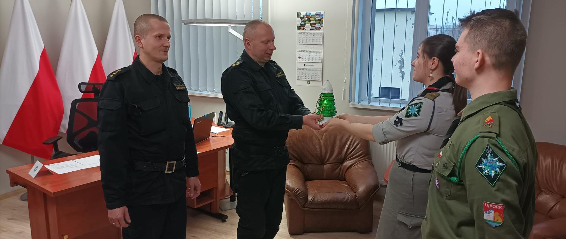 Zdjęcie przedstawia harcerzy przekazujących Komendantowi Powiatowemu PSP w Lęborku Betlejemskie Światło Pokoju.
