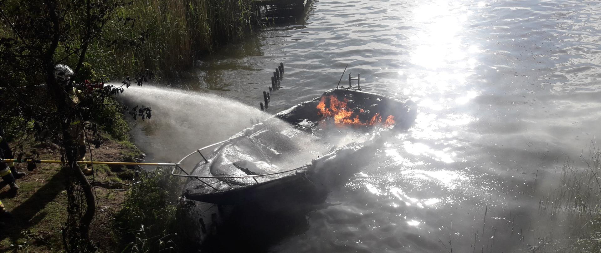 Jezioro, paląca się łódź, strażacy gaszący pożar