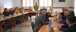 Komendant Powiatowy PSP Skarżysko-Kamienna wita przybyłych gości na naradę roczną za rok 2022r. Wszyscy siedzą przy stołach na świetlicy KP PSP Skarżysko.