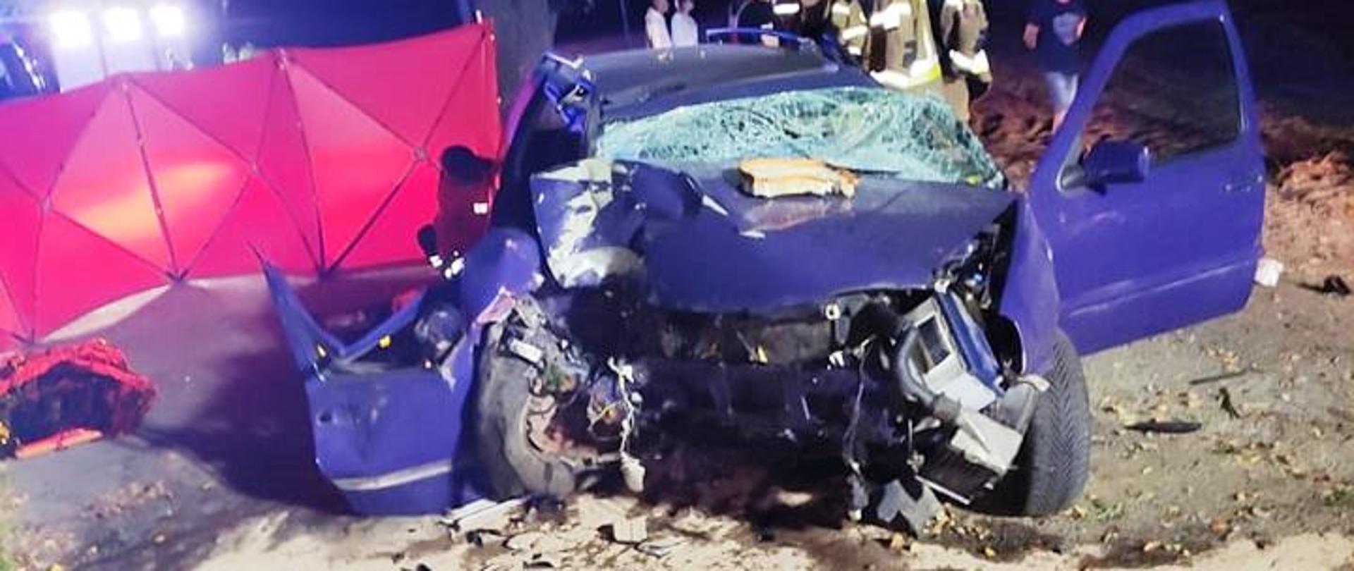 Zniszczony przód samochodu osobowego, na drugim planie rozstawiony czerwony parawan