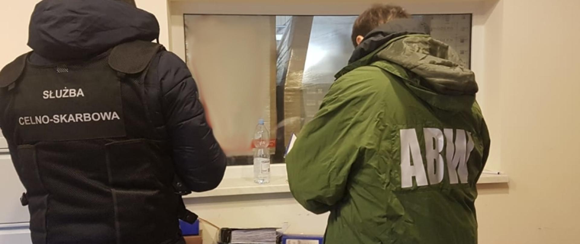 Funkcjonariusz KAS i funkcjonariusz ABW stoją tyłem, przed nimi segregatory.