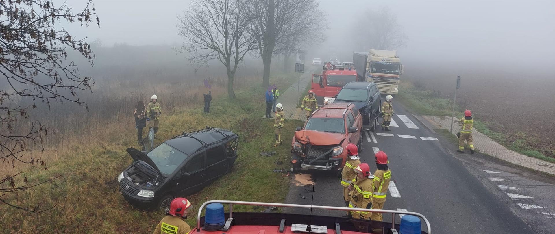 Zdjęcie zrobione z dachu samochodu pożarniczego, jest pochmurnie i mglisto. Na zdjęciu widać dwa samochody po zderzeniu w okolicy przejścia dla pieszych. Jeden samochód po zdarzeniu zjechał do przydrożnego rowu natomiast drugi zatrzymał się na jezdni