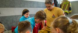 Strażak instruuje dzieci, które ćwiczą resuscytację krążeniowo-oddechową na fantomie podczas zajęć edukacyjnych