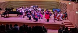 Grająca Orkiestra smyczkowa i śpiewający chór PSM I i II st. na scenie sali koncertowej z dyrygentką w stroju diabła