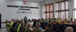Uczestnicy spotkania koordynacyjnego służb mundurowych przy stole konferencyjnym w budynku przejścia granicznego w Korczowej. W wydarzeniu biorą udział przedstawiciele straży granicznej, policji, wojska i straży pożarnej.
