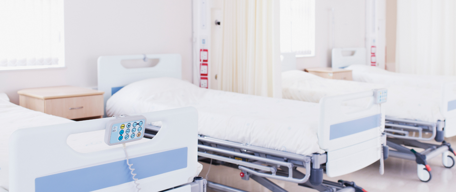 cztery białe łóżka na kółkach z białą pościelą, oddzielone zasłonami