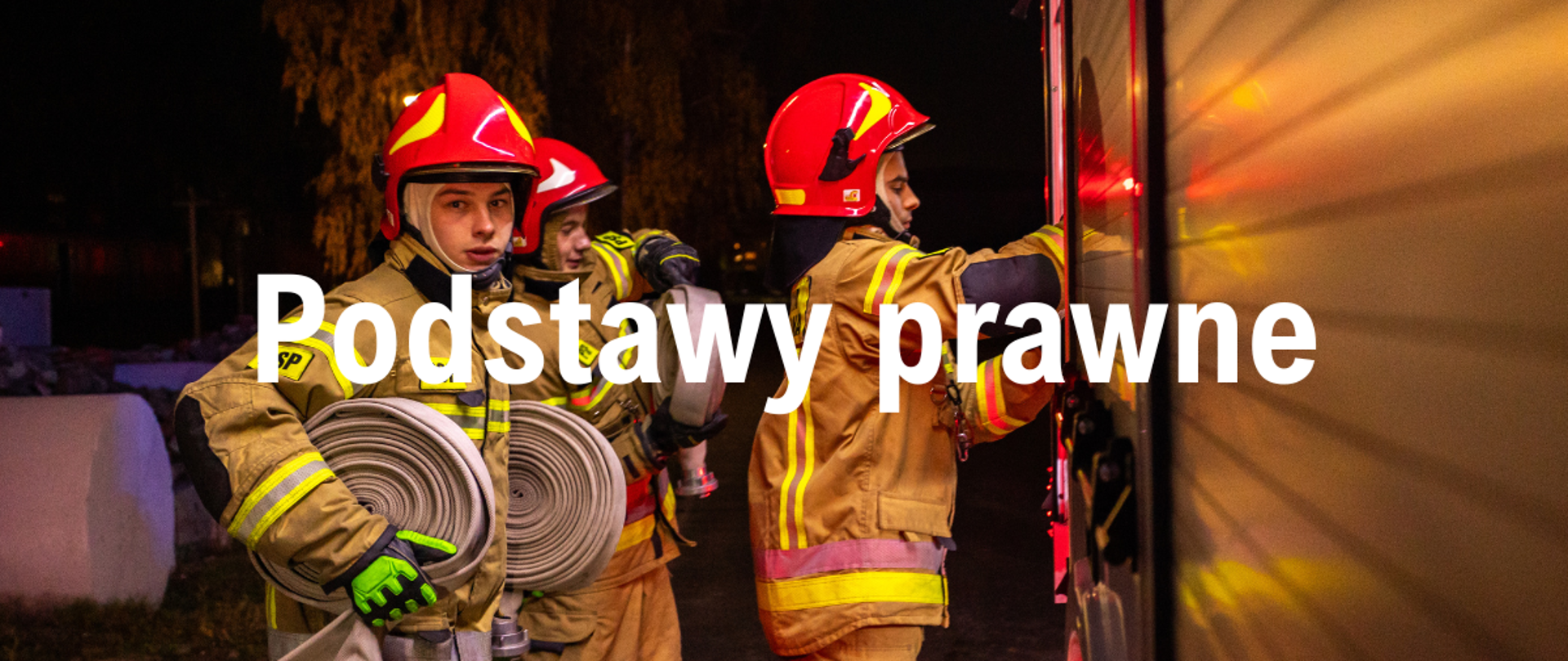 Trzech strażaków z wężami zwiniętymi w krąg stoją przy samochodzie pożarniczym. 