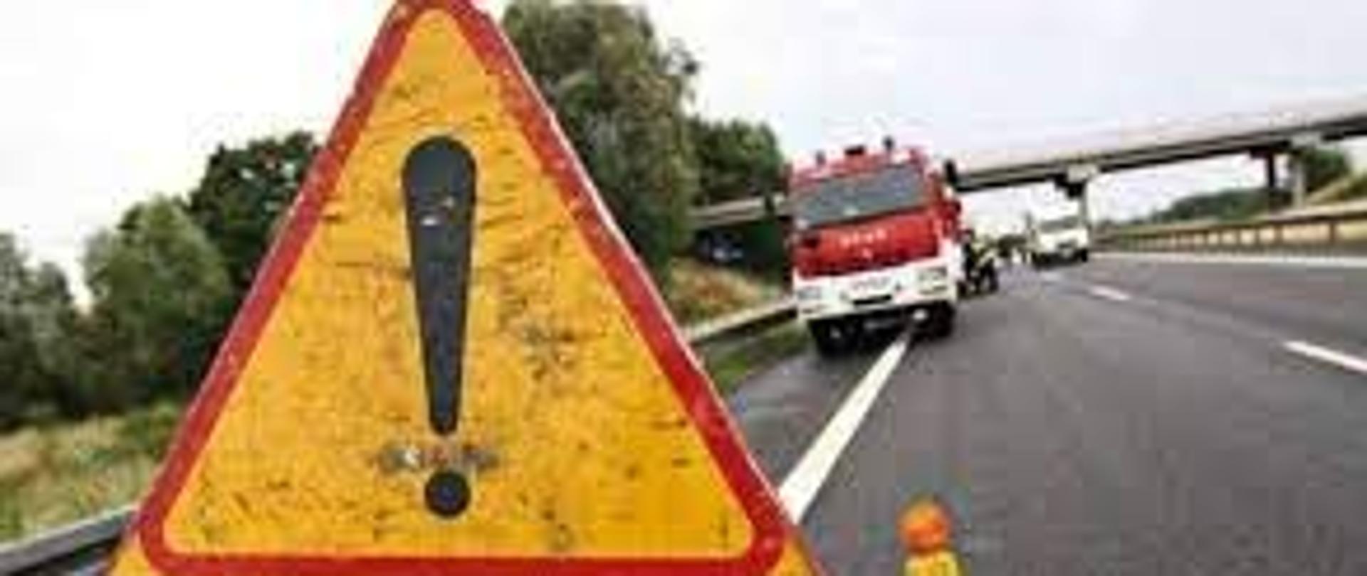znak ostrzegawczy z napisem wypadek a w tle samochód strażacki