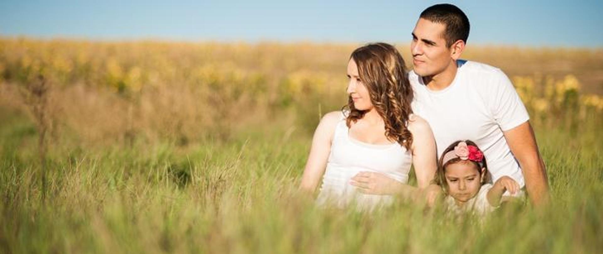 rodzina na wsi - kobieta, dziecko i mężczyzna siedzą w trawie