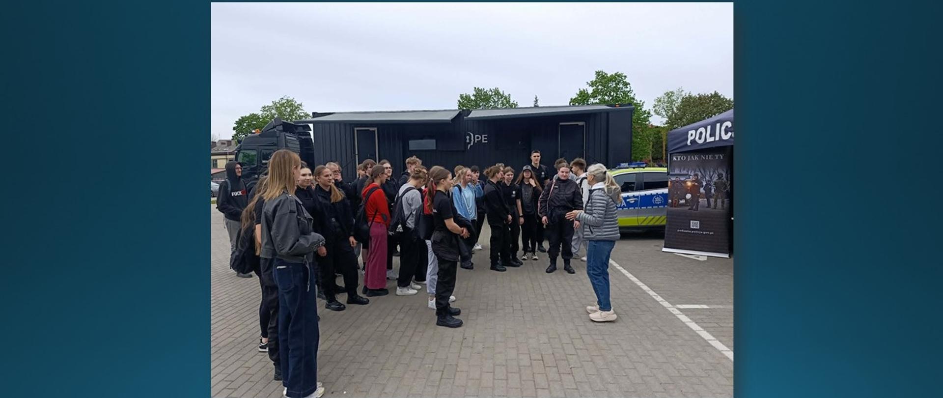 Grupa uczniów słuchających prelekcji wygłaszanej przez kobietę.