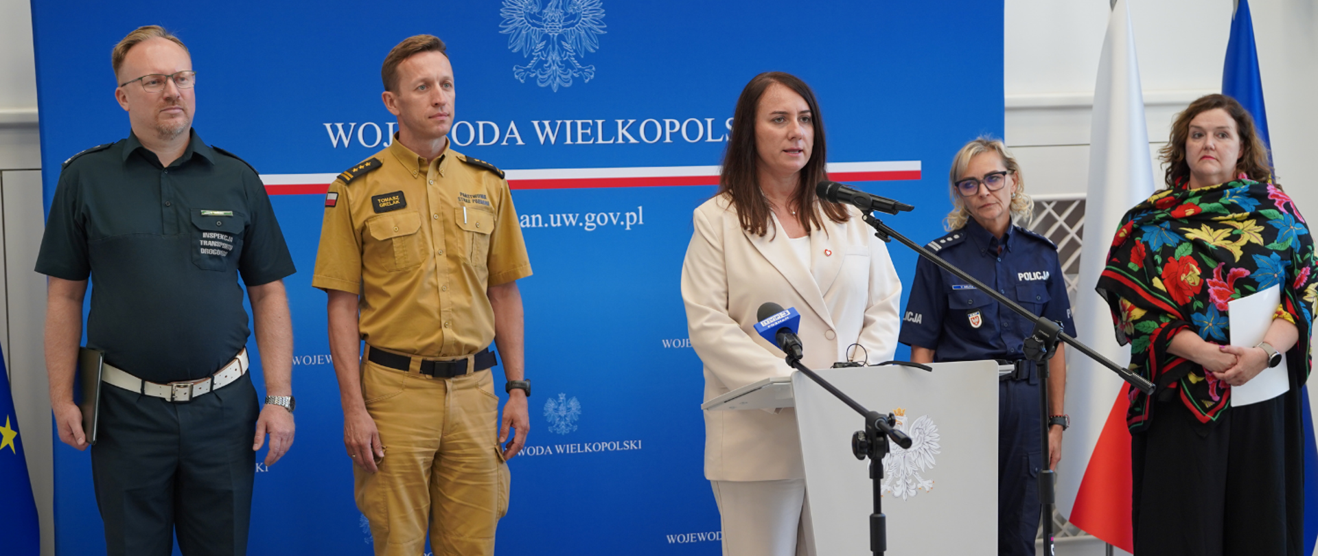 Wicewojewoda przemawia stojąc pośrodku sali, za nią pozostali przedstawiciele instytucji, jest przy mównicy, mówi do mikrofonu. 