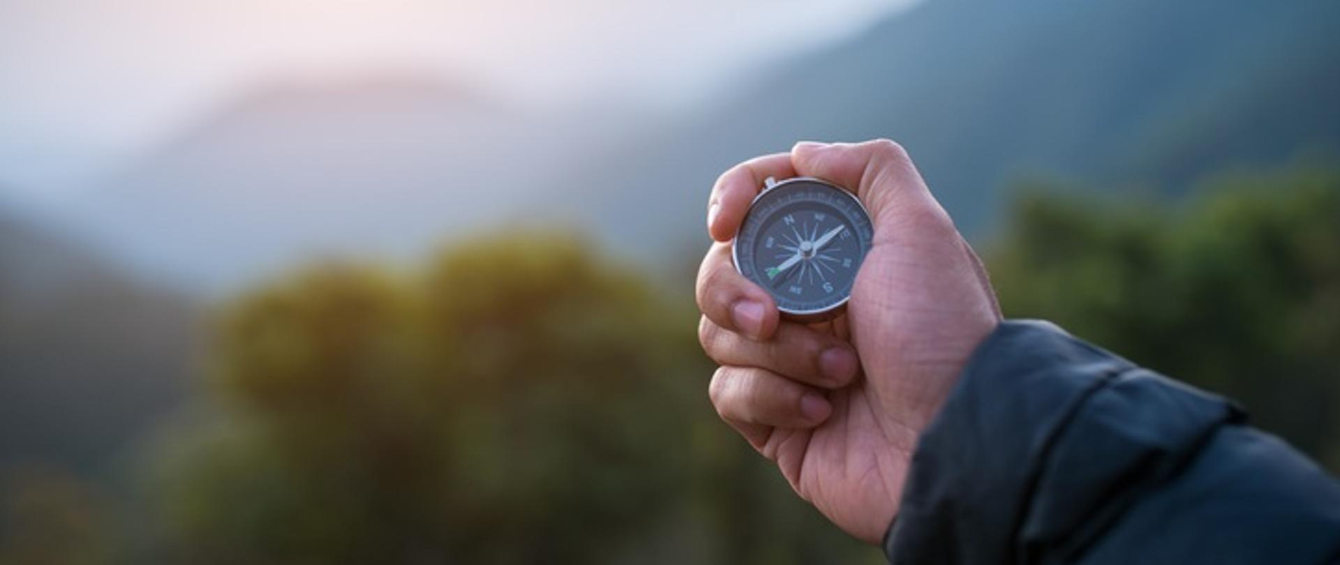 Męska ręka z kompasem na tle gór.