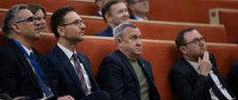 Minister rozwoju i technologii Waldemar Buda siedzi w auli, po jego prawej stronie siedzi ambasador Ukrainy w Polsce Andrij Deszczyca, zaś po lewej prezes Polskiej Agencji Inwestycji i Handlu Krzysztof Drynda.