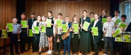 Grupa starszych uczniów na scenie sali kameralnej psm w rękach trzymają dyplomy i instrumenty